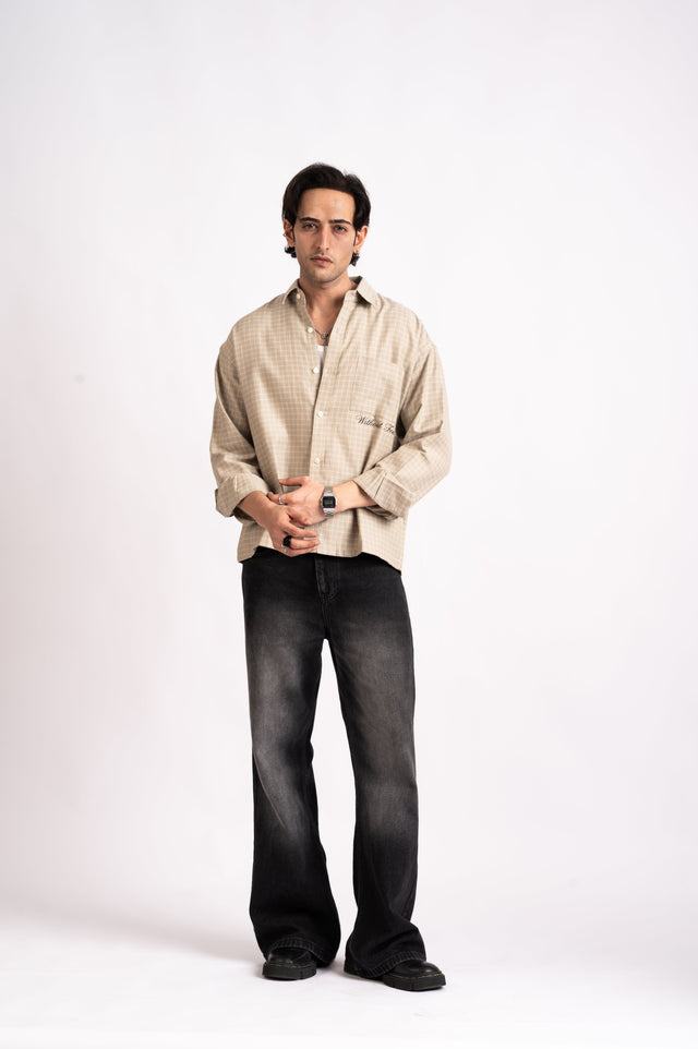 A man wearing a Nomad Check Boxy Shirt- Beige in a relaxed-fit cropped style over a white undershirt with black wide-leg jeans.
