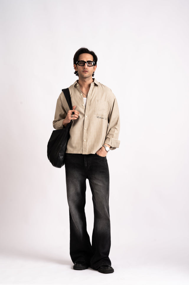 A person wearing a beige Nomad Check Boxy Shirt, a relaxed-fit cropped shirt, and black wide-leg jeans, carrying a black shoulder bag.