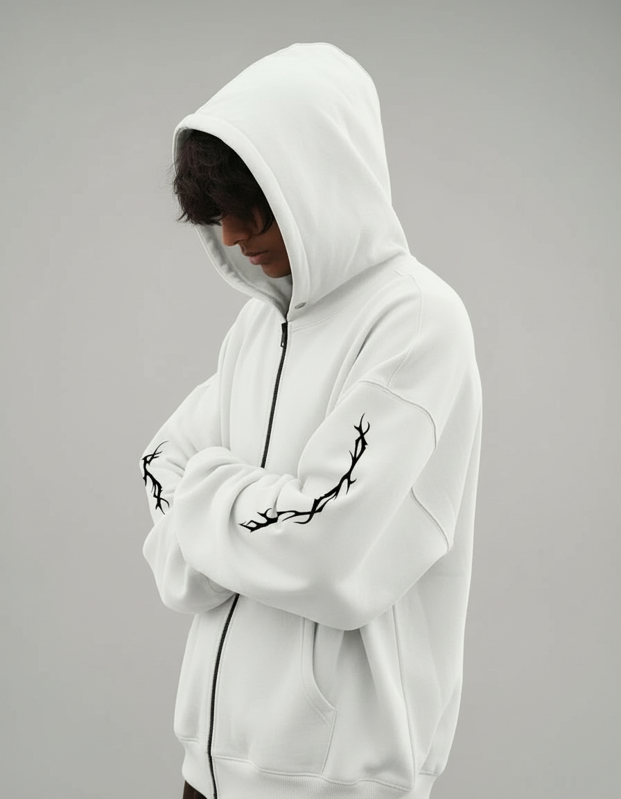 Person wearing a white hoodie with black tribal designs on the sleeves against a dark background
