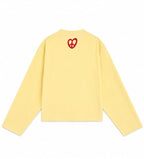 A pale yellow long-sleeve crewneck sweatshirt shown from the back, featuring a small red heart-shaped peace sign graphic centered on the upper back.