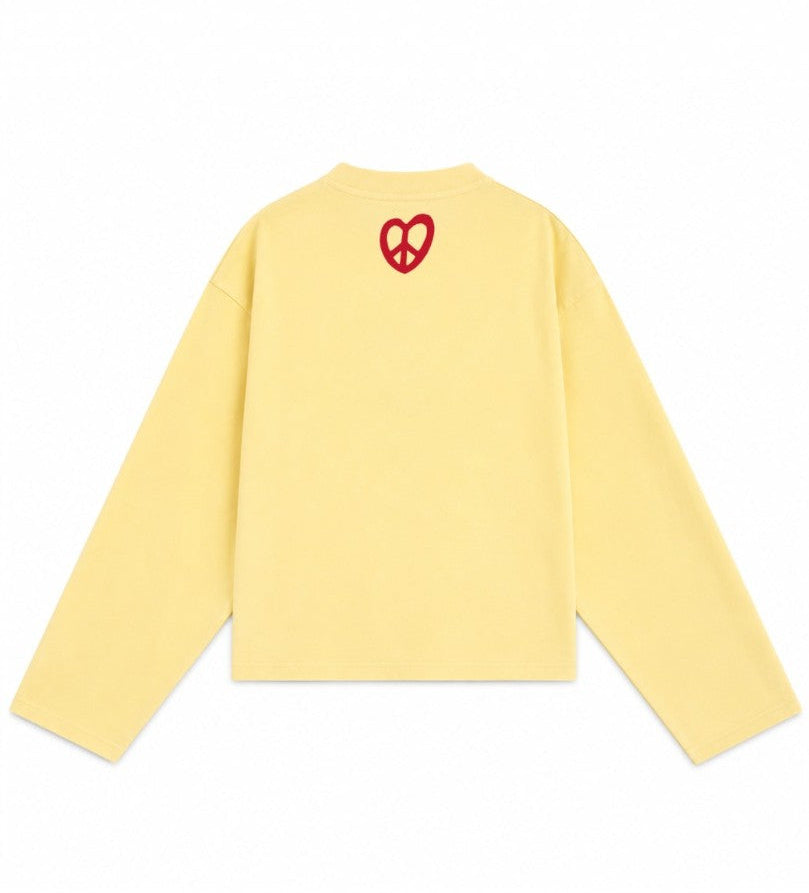 A pale yellow long-sleeve crewneck sweatshirt shown from the back, featuring a small red heart-shaped peace sign graphic centered on the upper back.