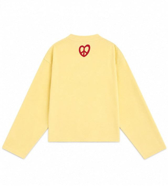 A pale yellow long-sleeve crewneck sweatshirt shown from the back, featuring a small red heart-shaped peace sign graphic centered on the upper back.